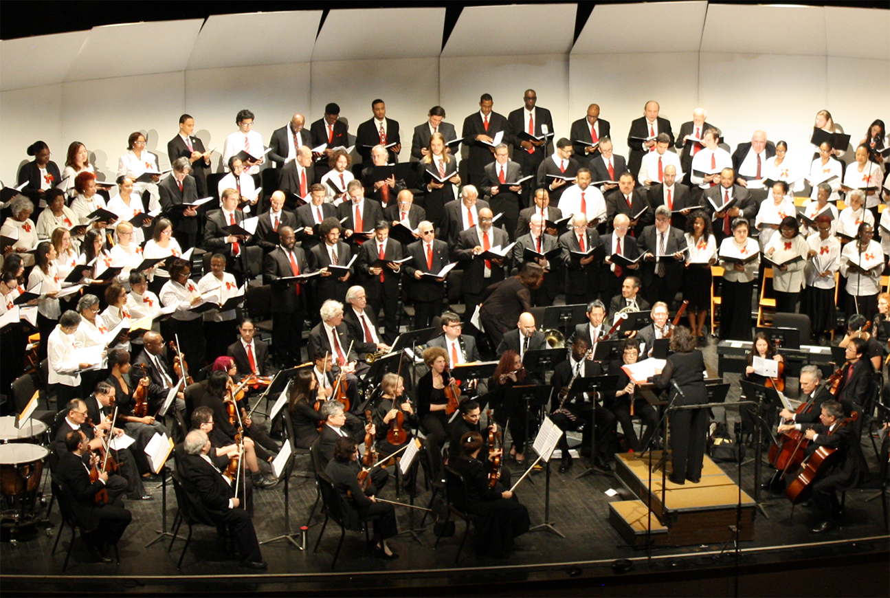 A large choir and orchestra performing together on stage under a conductor.