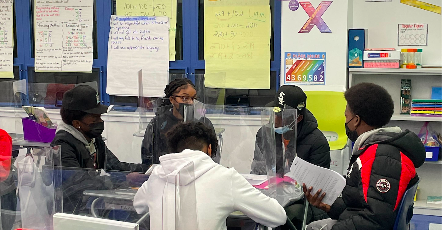 Young people sitting in a circle in a classroom, wearing masks.