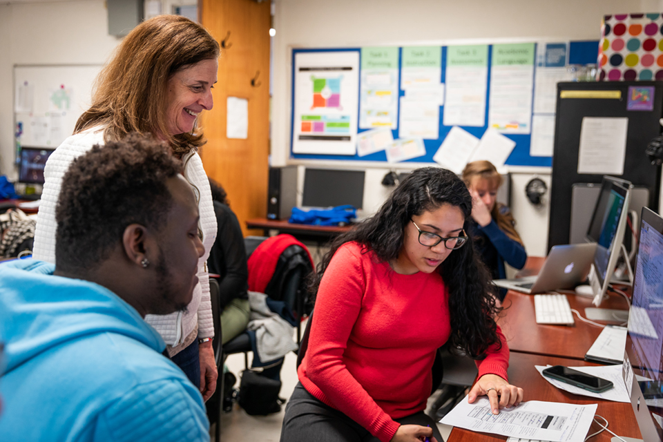 A woman standing next to students sitting at desks.