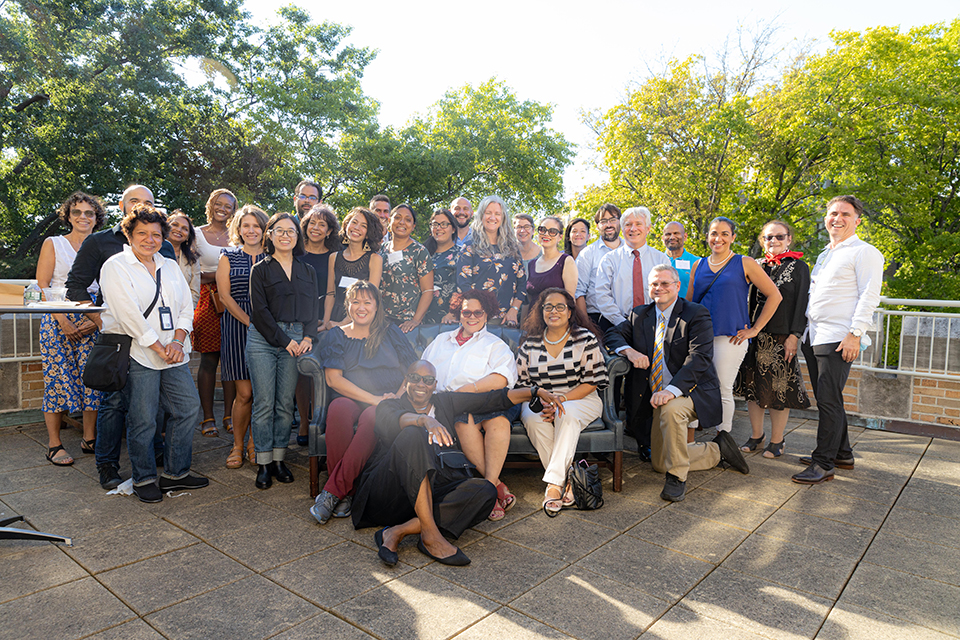 A group of approx. 30 adults posing on a patio. There are trees in the background.