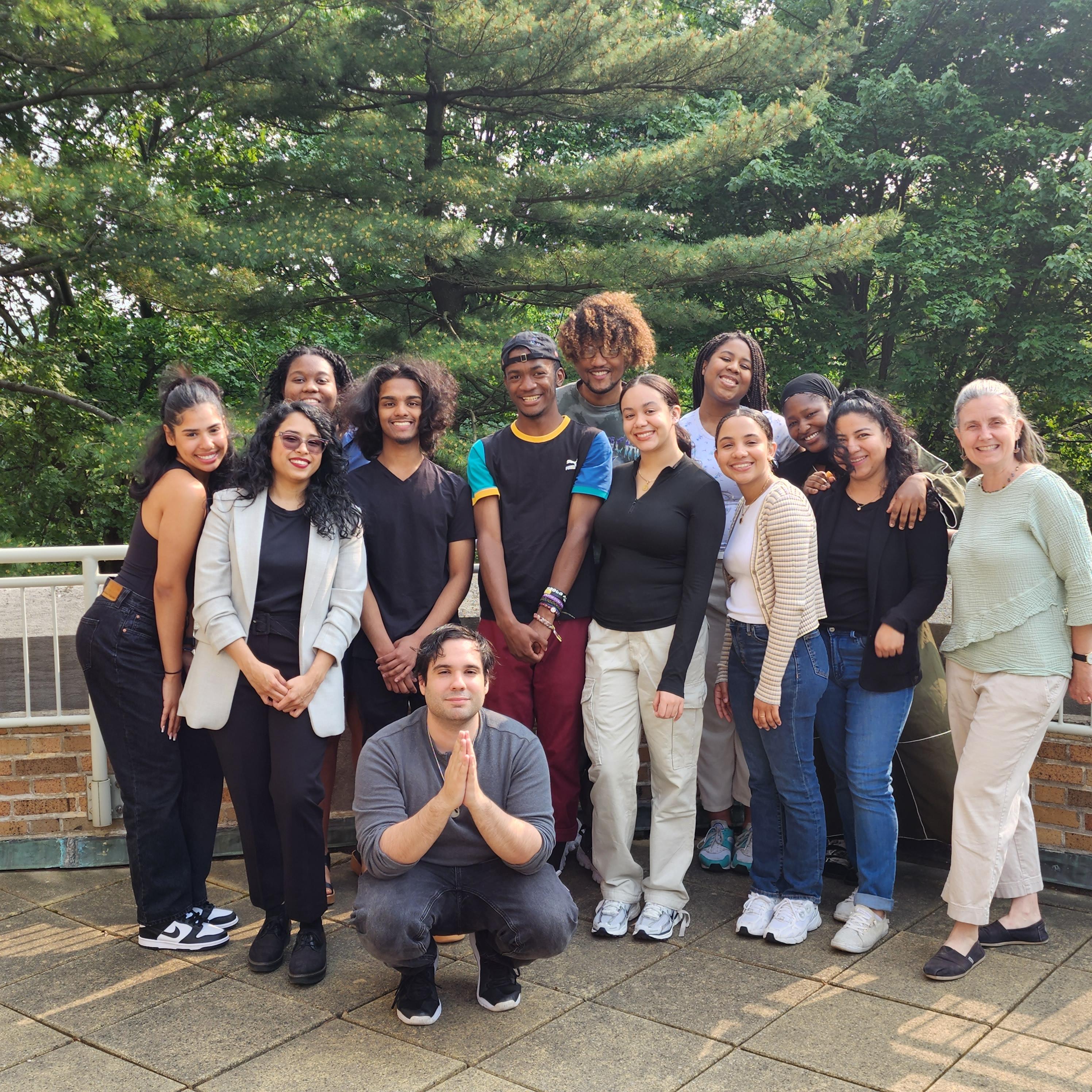 A diverse group of students poses with trees in the background.