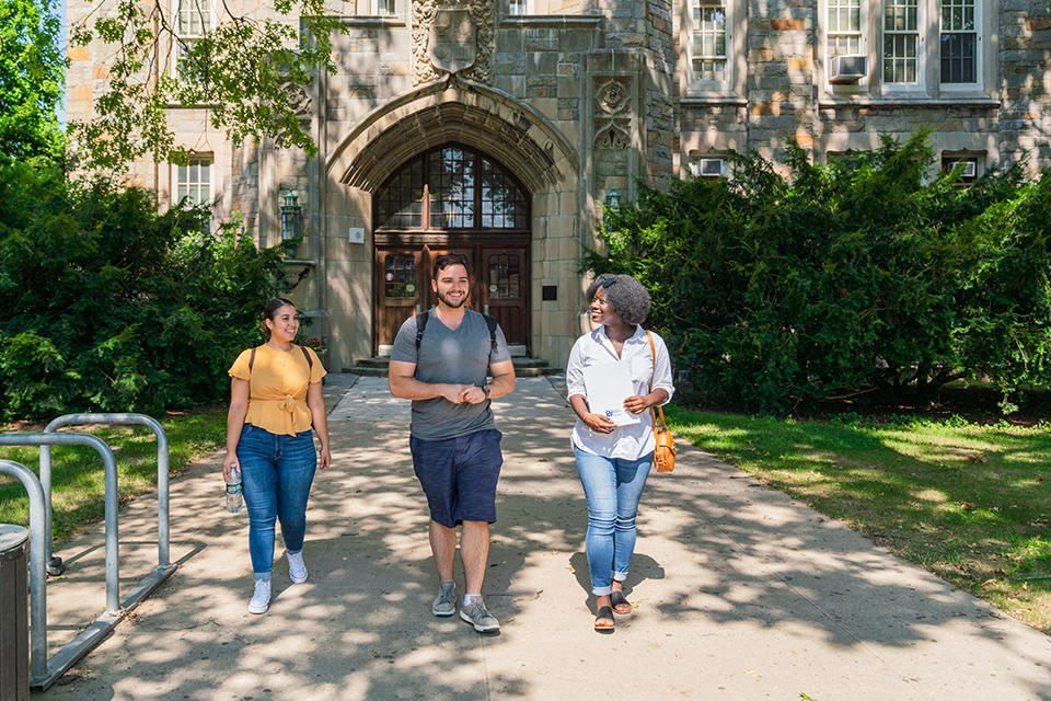 Three students walking in front of a college building.