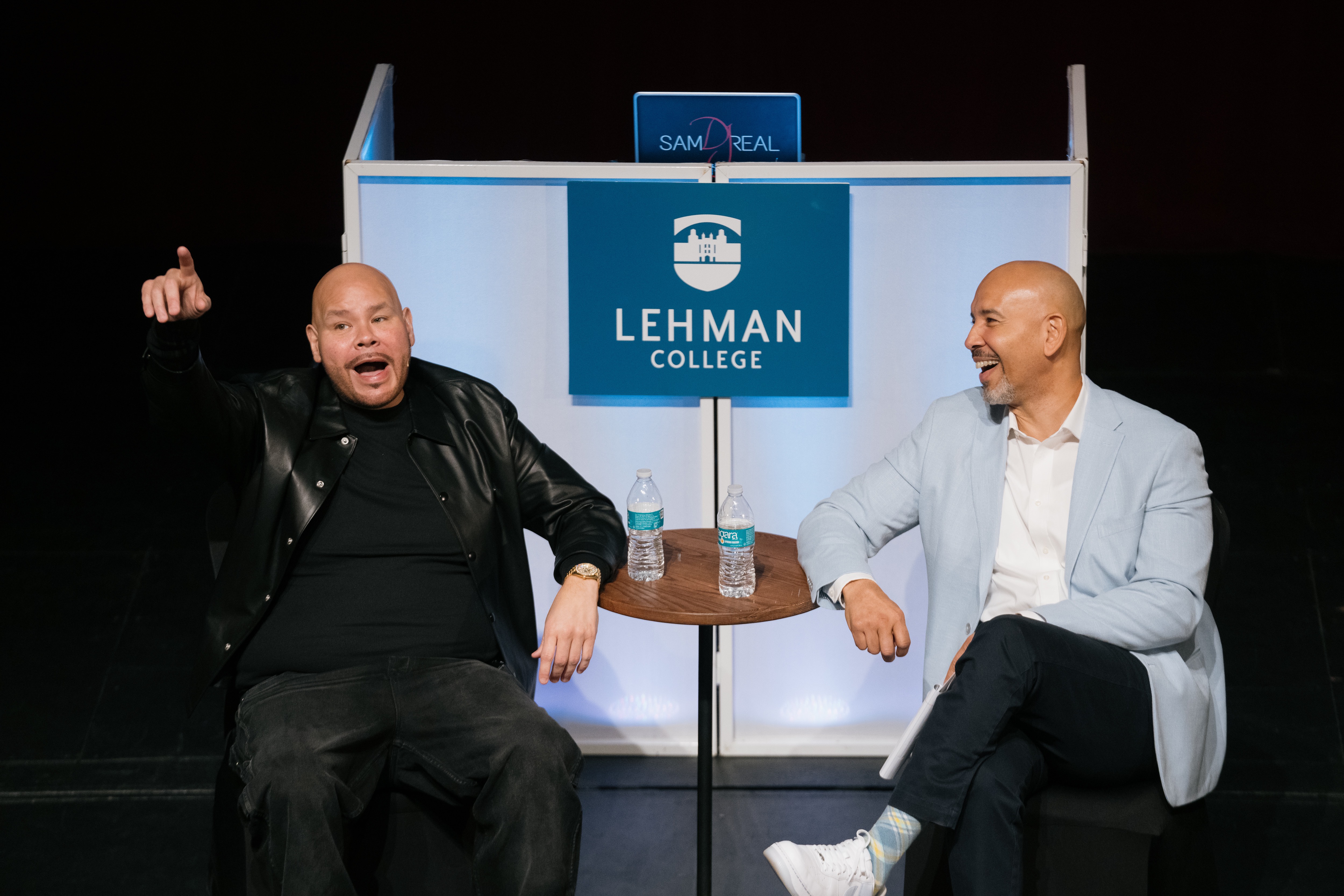 Fat Joe and Ruben Diaz Jr sit on a stage talking. Fat Joe is pointing to the audience.