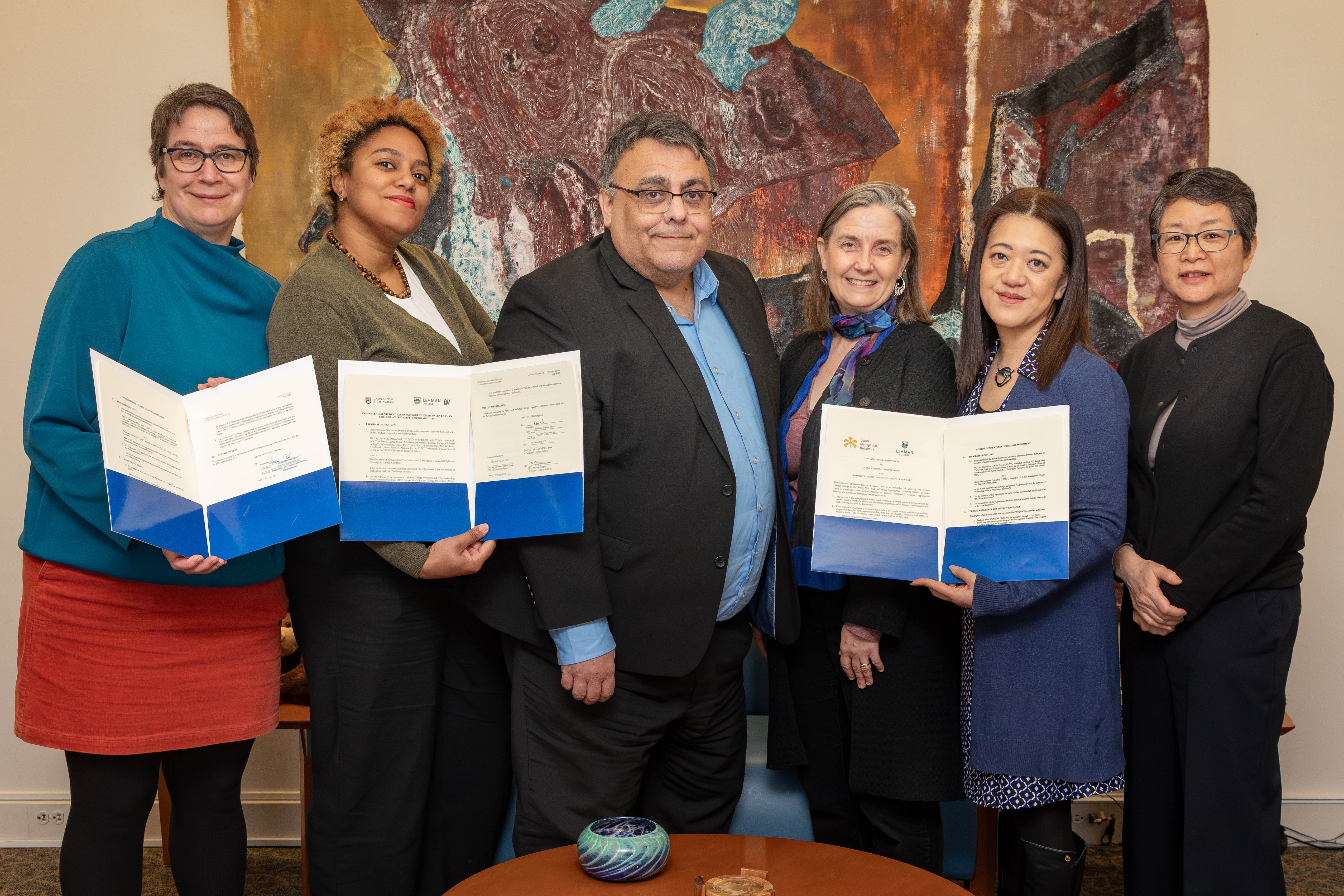 A group of five people stand together holding documents.