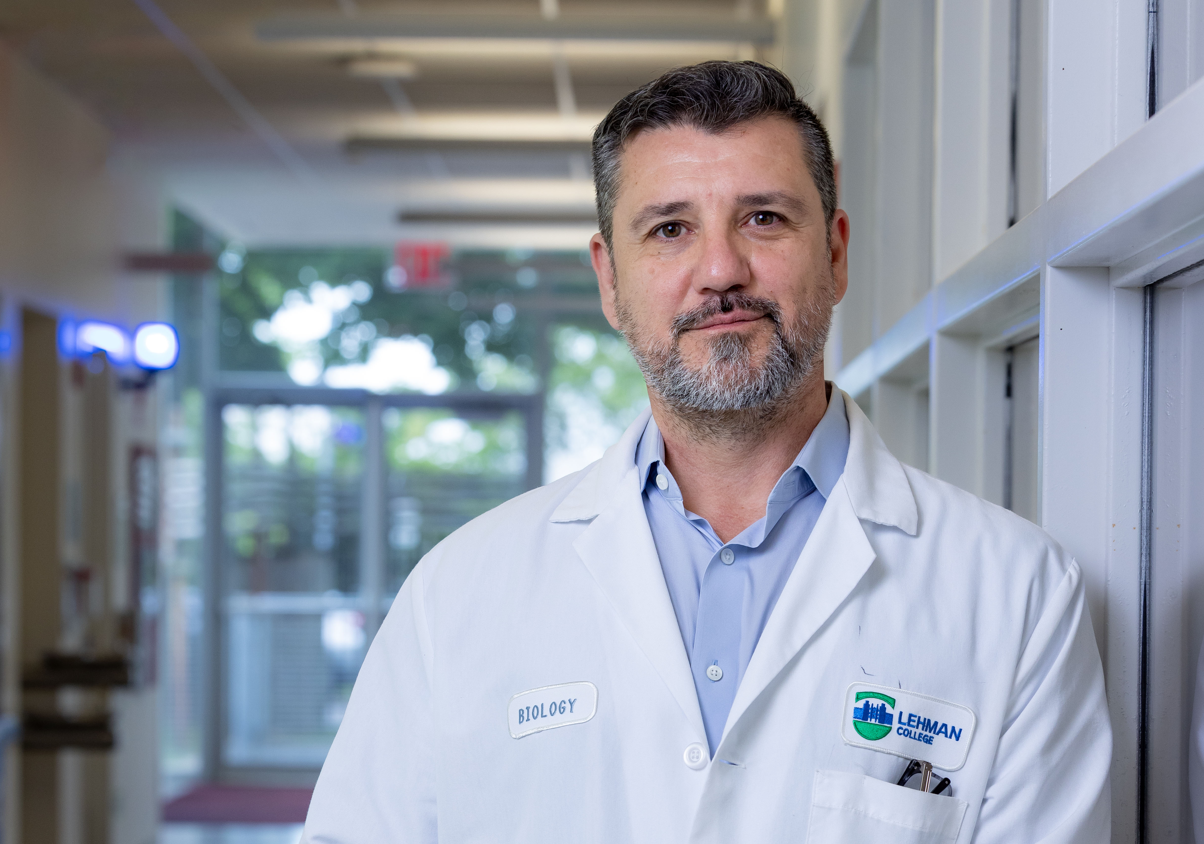Portrait of a man in a lab coat in a building hallway.