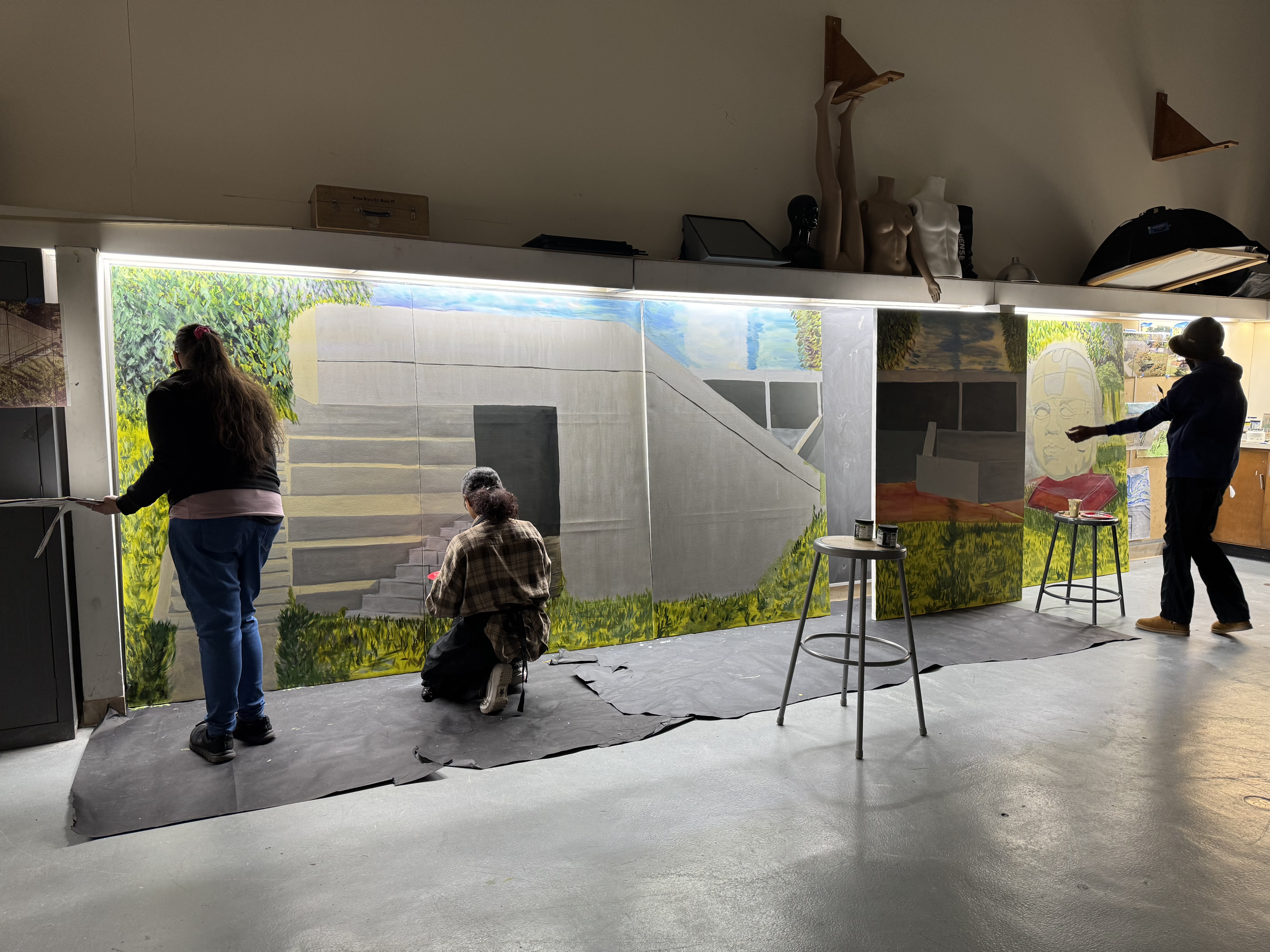 Three people working on a mural in an art studio.