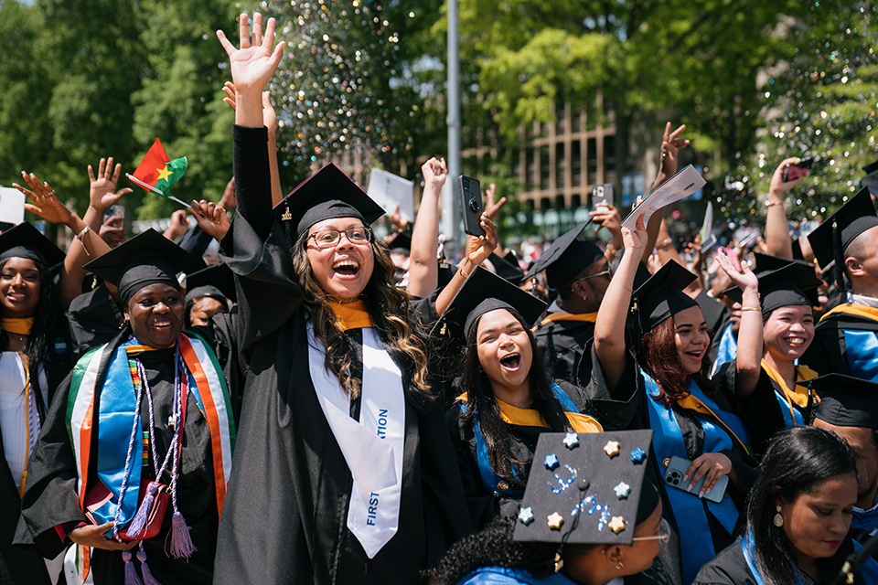 Students in regalia waving arms and throwing confetti.