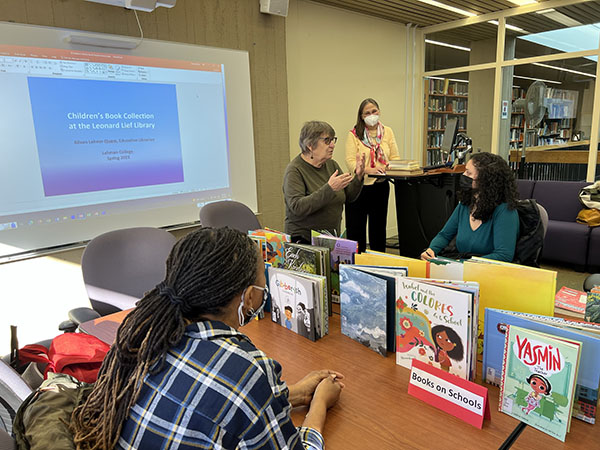 College class visitin the library with faculty and librarian with children's books on table